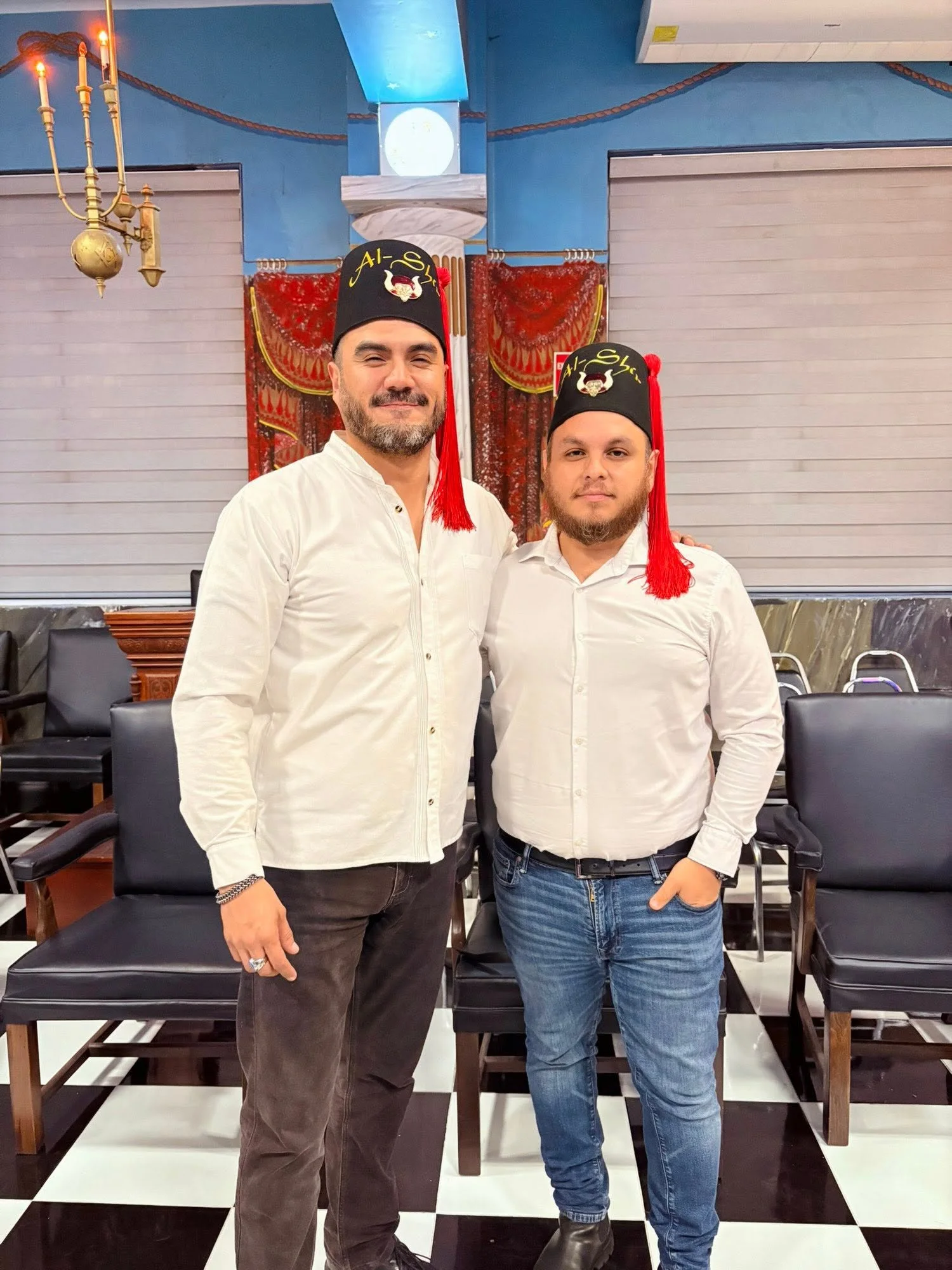 Dos participantes con fez y camisa blanca.